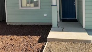 Una casa de un piso con puerta azul, una ventana pequeña y un porche de concreto.