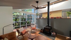 Un salon moderne doté d’une grande porte vitrée donnant sur un jardin, d’un banc en bois, d’une petite table ronde et d’un poêle à bois.