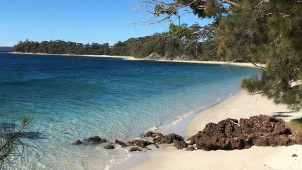Une plage avec une eau d’un bleu limpide, un rivage sablonneux et des affleurements rocheux.