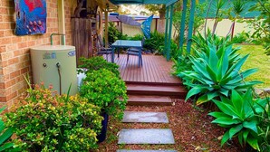 A garden patio with a table and chairs, surrounded by lush greenery and a brick wall.
