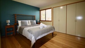 A bedroom with a wooden bed, a nightstand, a window, and a wardrobe. - Waterfront Hideaway by Book Jervis Bay - Sanctuary Point - The Ultimate Spot to Relax (Sanctuary Point)