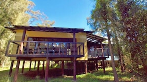 A two-story wooden structure with a balcony, surrounded by trees. - Waterfront Hideaway by Book Jervis Bay - Sanctuary Point - The Ultimate Spot to Relax (Sanctuary Point)