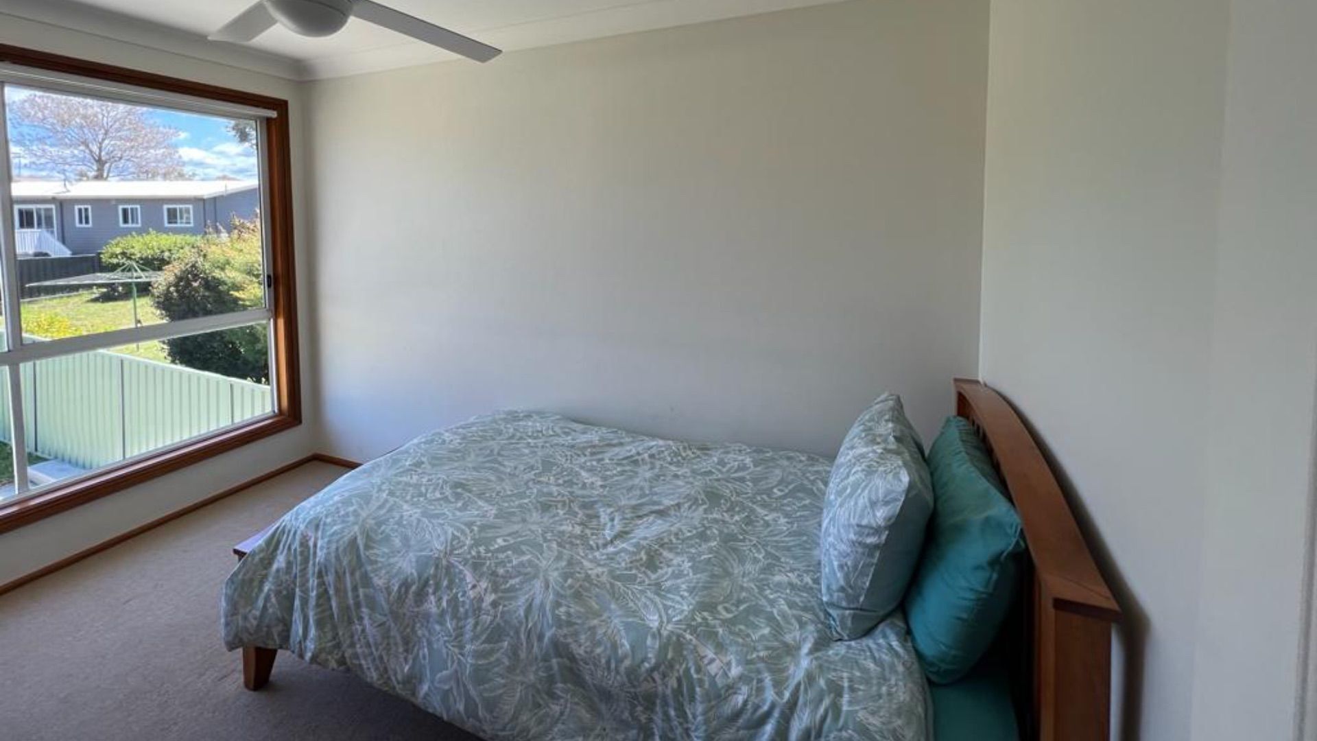 Un dormitorio con cama, ventana y vista a una casa vecina.