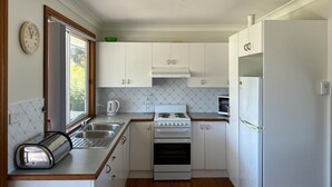 A compact kitchen with white cabinets, a stove, a sink, and a refrigerator. - Sanctuary 79 by Book Jervis Bay - Family home located in Sanctuary Point (Sanctuary Point)
