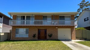 A two-story residential building with a front garage, a small front yard, and a balcony with a white railing. - Sanctuary 79 by Book Jervis Bay - Family home located in Sanctuary Point (Sanctuary Point)