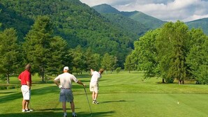 Un campo de golf con tres jugadores, césped verde exuberante, árboles y montañas al fondo.