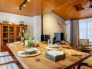 A dining area with a long wooden table set for a meal, a wooden cabinet with glass doors, a television, and a fireplace.