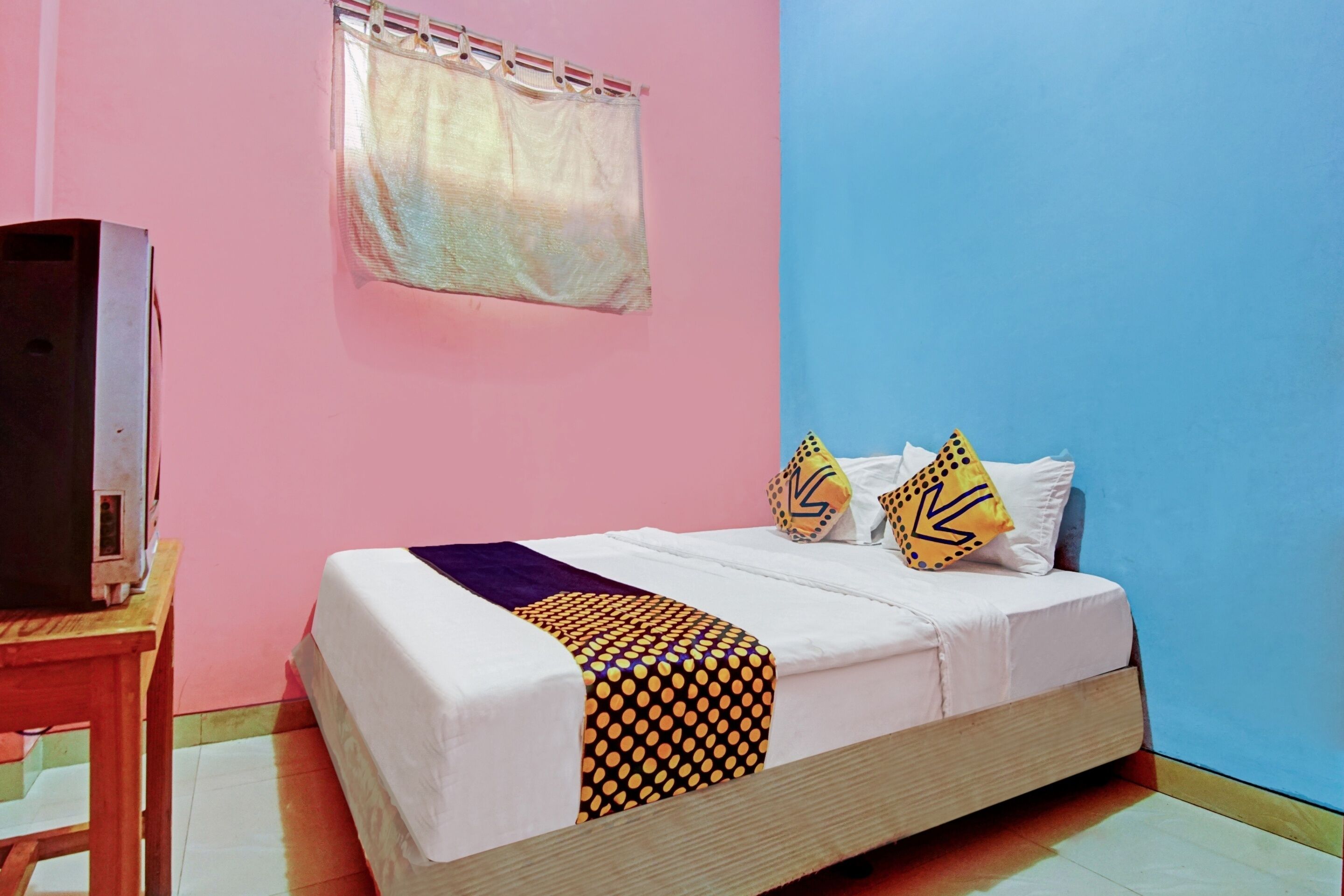 A room with a bed, a television on a wooden table, and a window with a curtain.