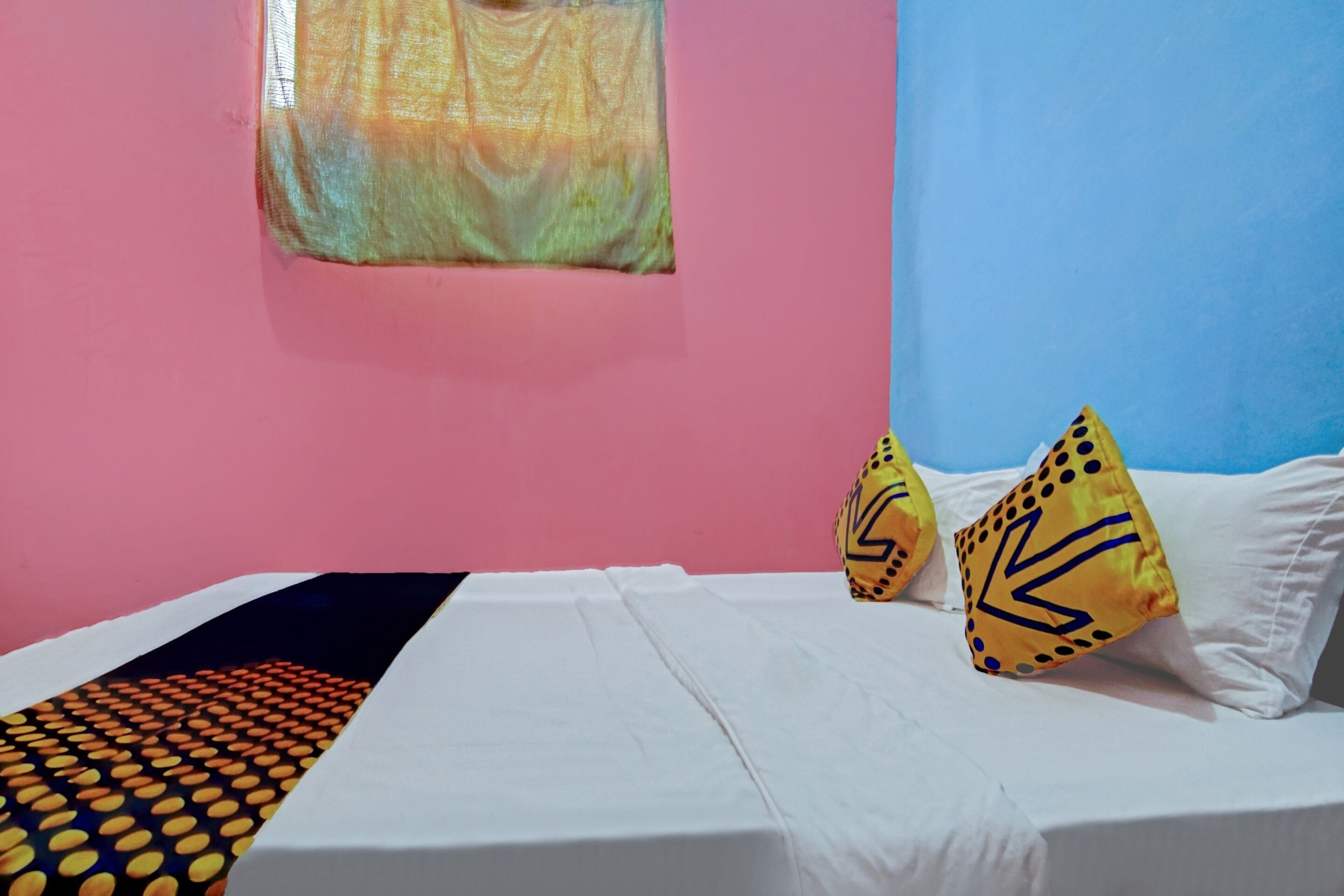 Una cama con ropa de cama blanca, dos almohadas con diseños amarillos y negros, y una pared rosa con una ventana.