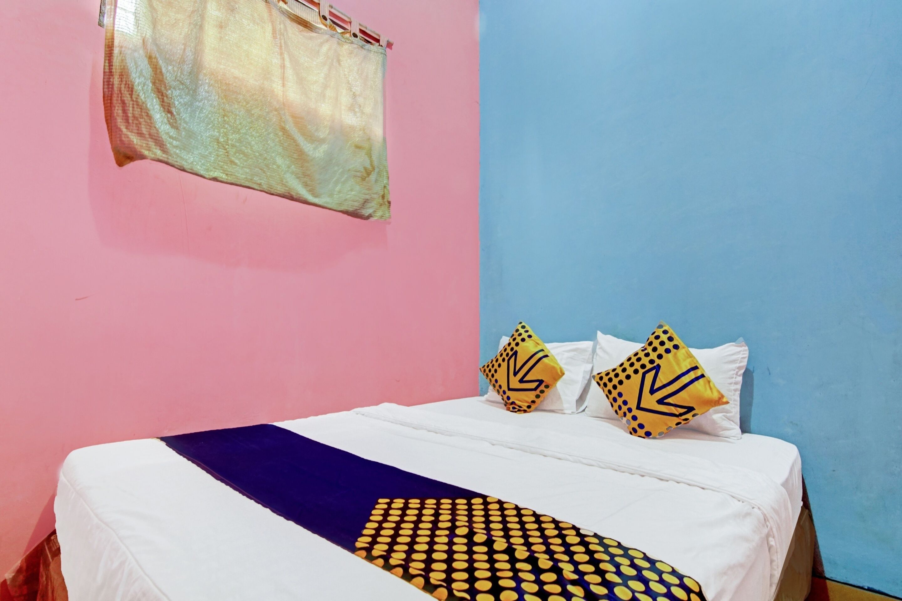 A bed with white bedding, two pillows with yellow and black patterns, and a blue wall.