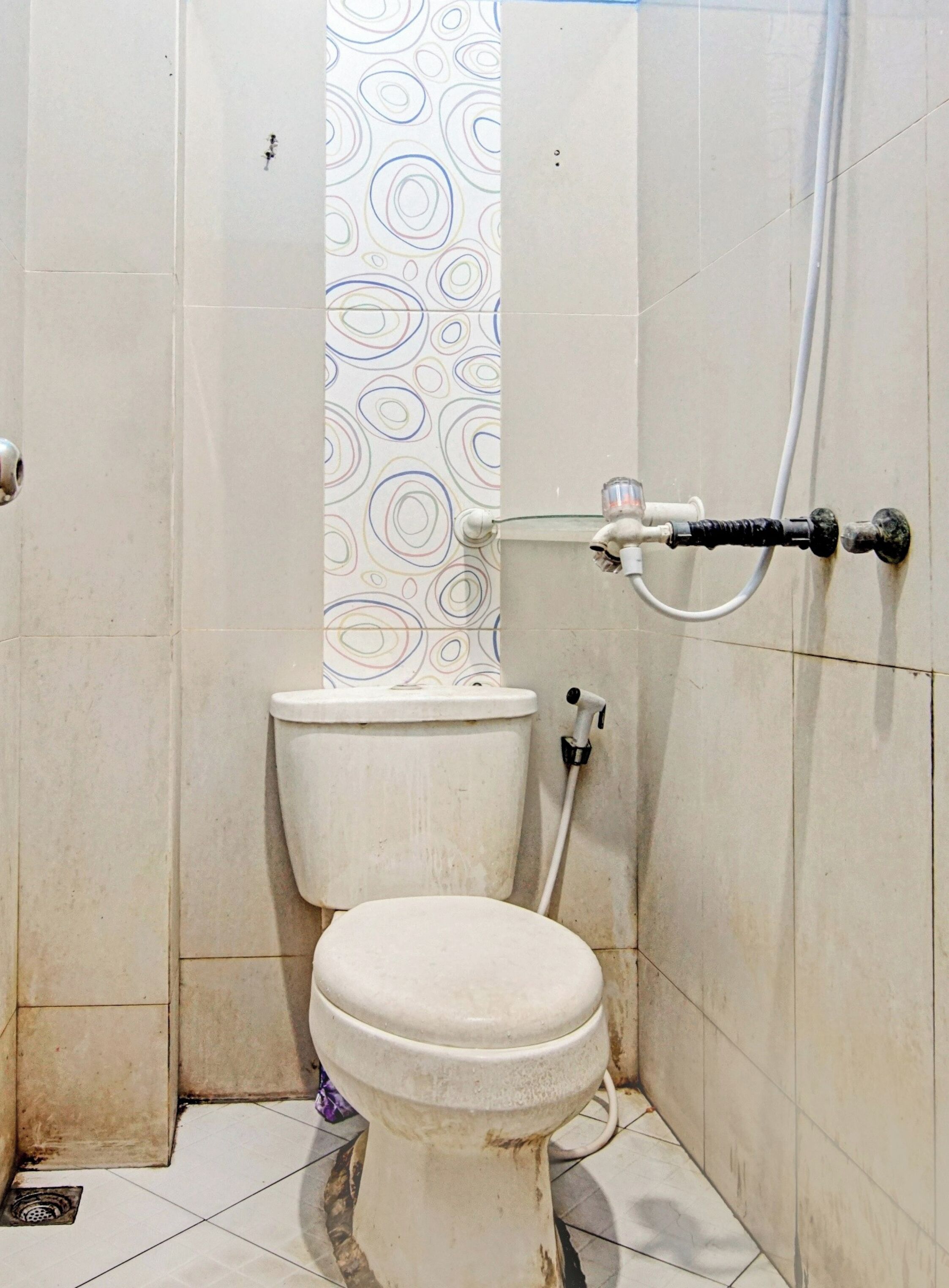 A small, narrow bathroom with a toilet, a shower, and a wall with a circular pattern.