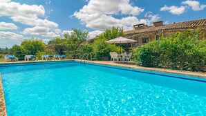 A clear blue swimming pool with lounge chairs and a table with an umbrella, surrounded by greenery and a building with a tiled roof. - SON MAYOL 1 - Fantastic private apartment in agroturismo, with shared pool and free Wifi (Felanitx)
