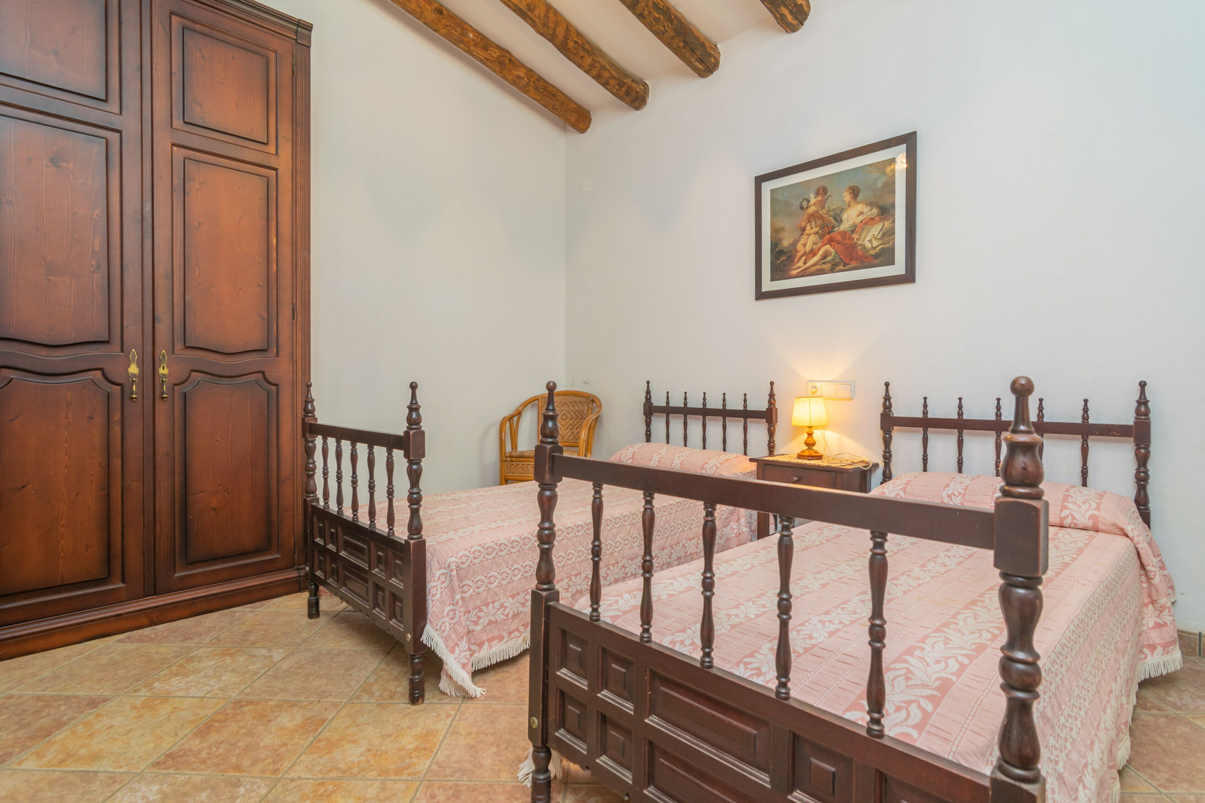 Un dormitorio con dos camas de madera, un armario, una silla y un cuadro en la pared.