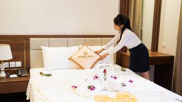 A hotel room with a neatly made bed, a pillow with the hotel name, a bedside phone, and a flower arrangement on the bed.