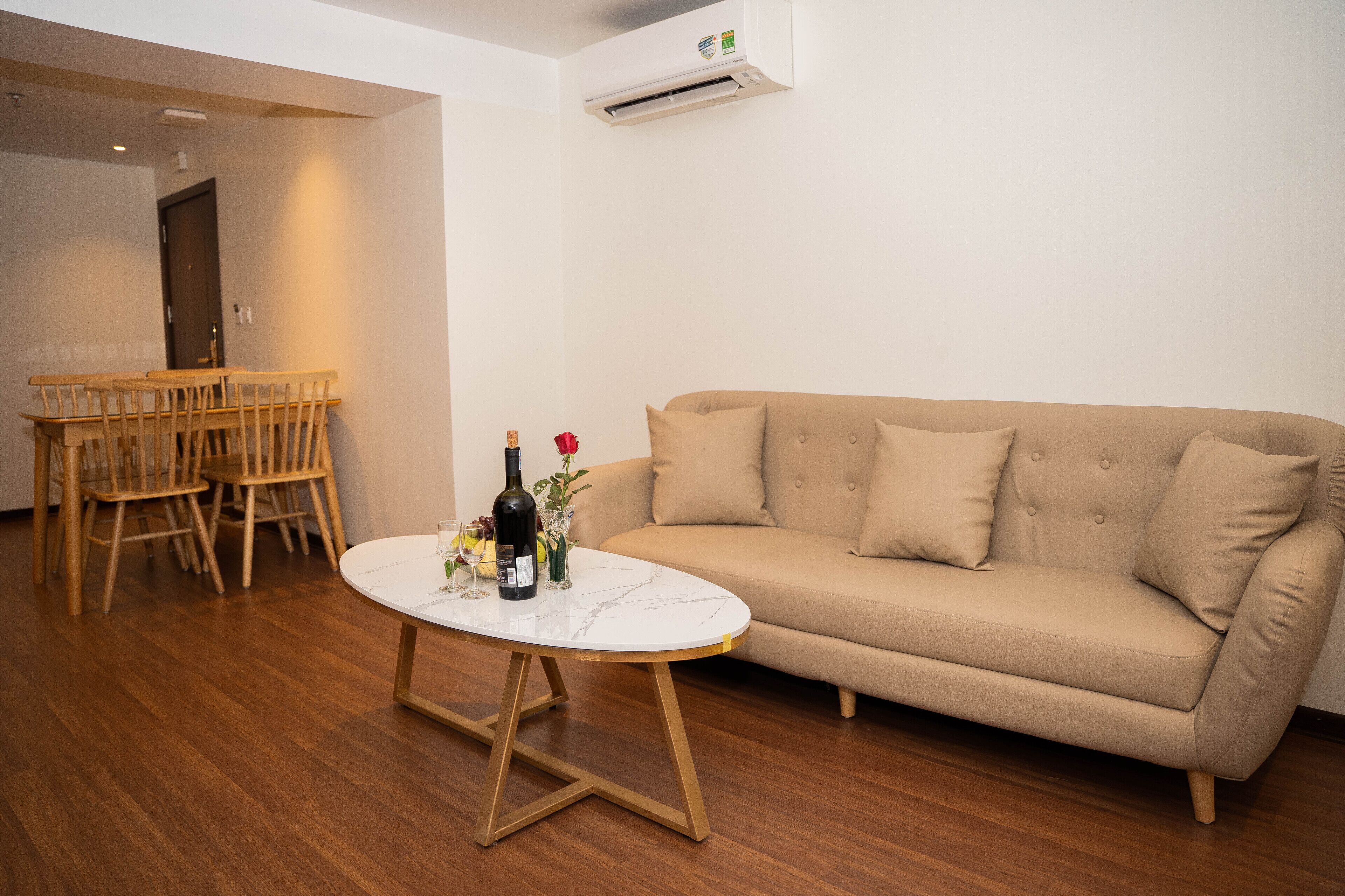 A living room with a beige sofa, a round coffee table, and a dining area with wooden chairs.