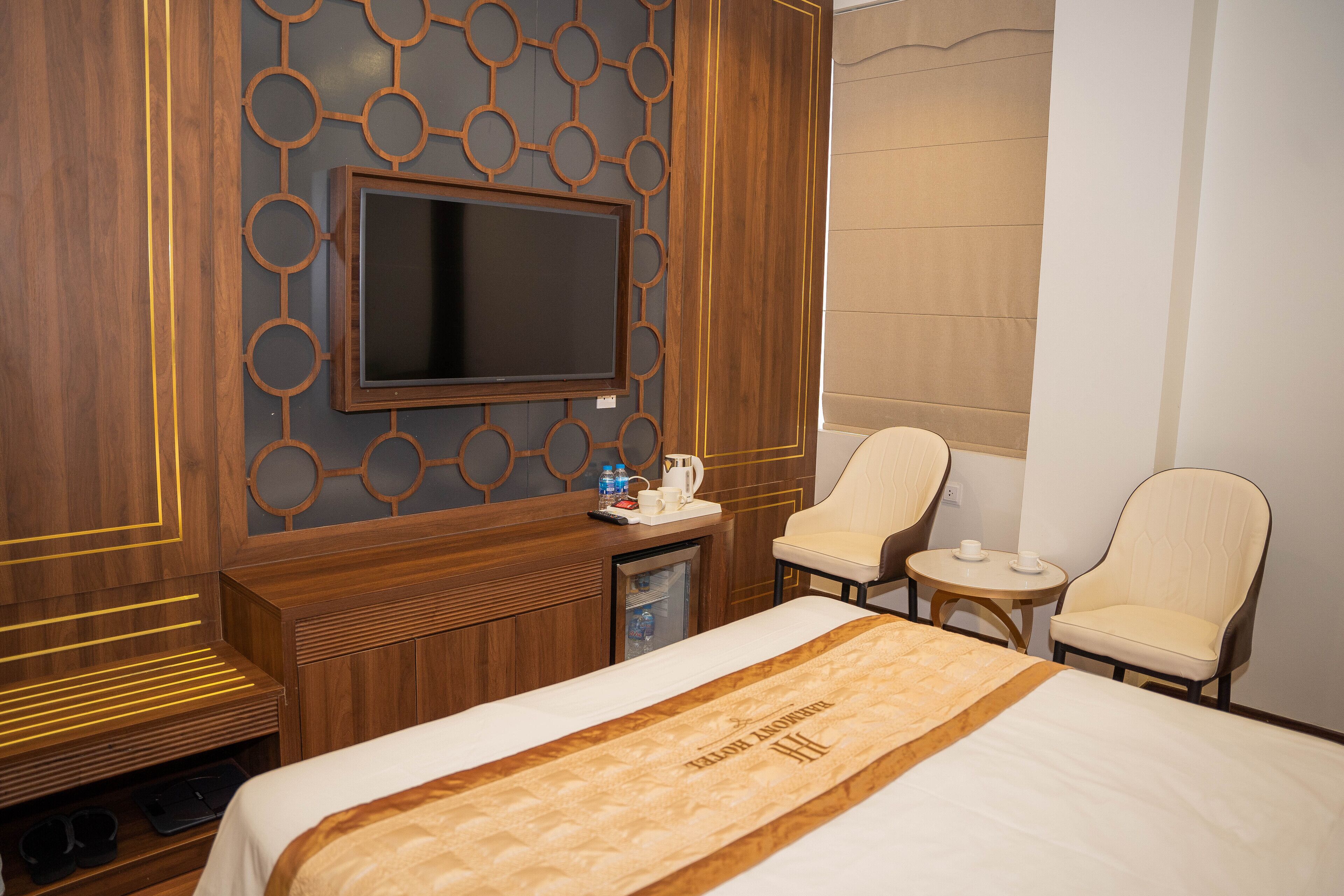 A hotel room with a large bed, a TV mounted on a wooden wall, a small desk with a chair, and two additional chairs.