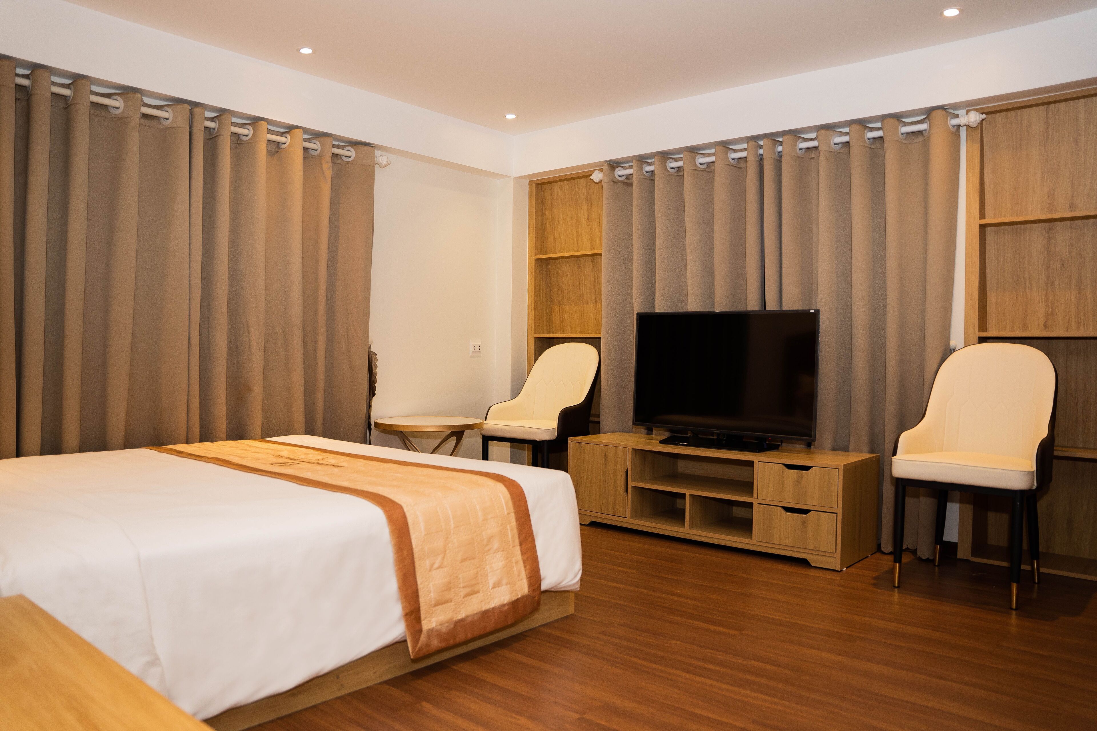A hotel room with a bed, a TV, two chairs, a wooden cabinet, and curtains.