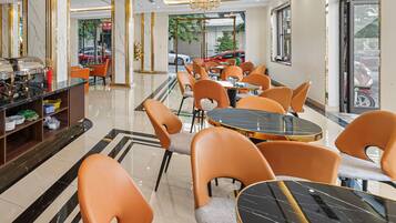 A modern hotel lobby with marble floors, orange chairs, and a central chandelier.