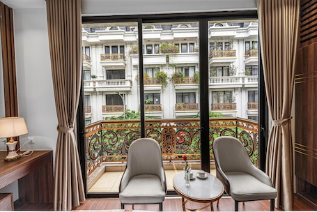 A balcony with ornate railings, two upholstered chairs, a small table, and a lamp.