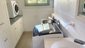 A compact, modern bathroom with a built-in washing machine, a sink, and a window providing natural light.