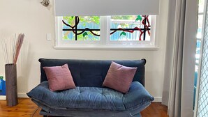 A dark blue sofa with two pink cushions, a tall striped vase, and a window with a view of greenery and a fence.