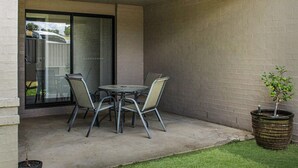 An outdoor patio with a round table and two chairs, a potted plant, and a glass door leading to a garage. - Quintet 1-157 - North Tamworth (Tamworth)