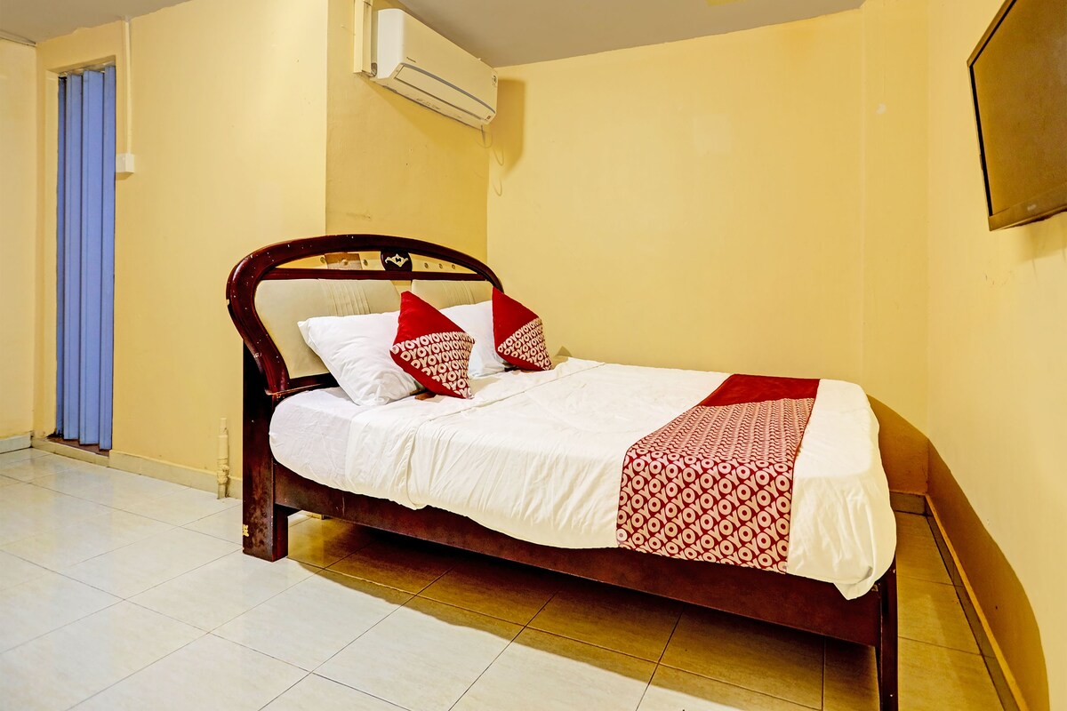 A single bed with a wooden frame, white bedding, and red patterned pillows in a room with yellow walls and a tiled floor.