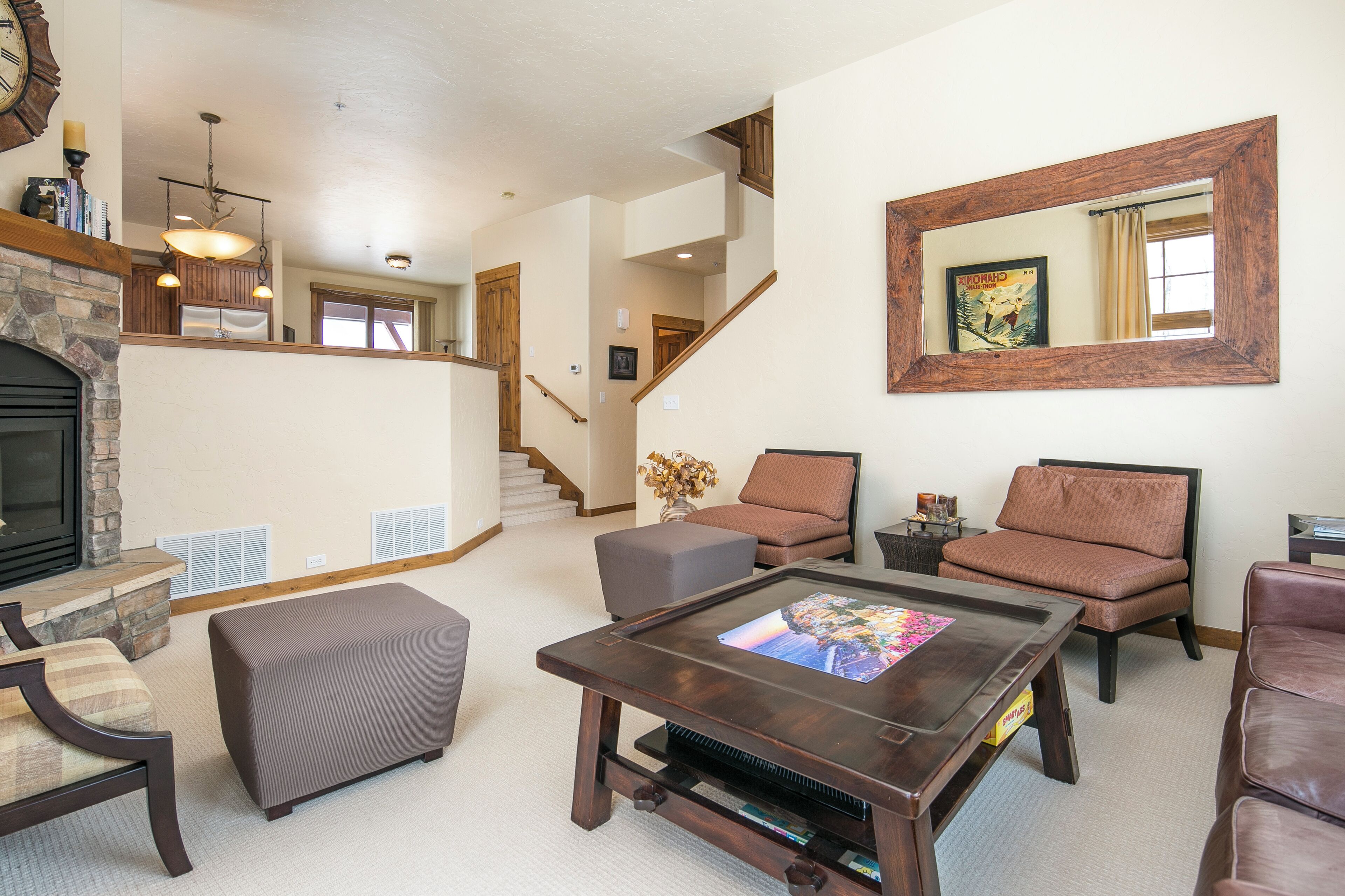 A spacious living room with a fireplace, comfortable seating, a large mirror, and a staircase leading to an upper level.