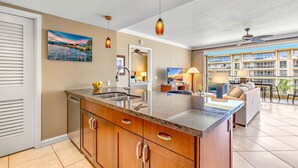 Une cuisine moderne dotée d’un grand îlot central, un coin repas avec un canapé et une table, et un balcon offrant une vue sur l’immeuble de l’hôtel.