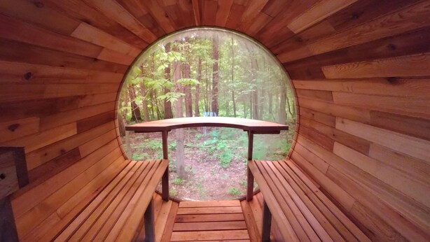 Una cabaña de madera circular con un banco y una mesa en el centro, rodeada de vistas al bosque.