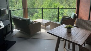 Un balcón con mobiliario de mimbre, una mesita y vistas a una zona boscosa.