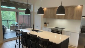 Una cocina moderna con una isla grande, taburetes negros, iluminación colgante y vistas a un patio exterior.