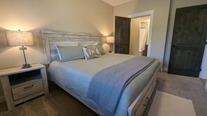 A bedroom with a bed, nightstands, a lamp, and a door leading to a bathroom.