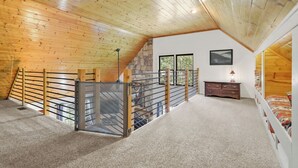 A bedroom with a sloped ceiling, a wooden staircase, a bed, a dresser, and a window with a view of greenery. - Creekfront! 5* Views, hot tub, fire pit, huge deck (Blue Ridge)