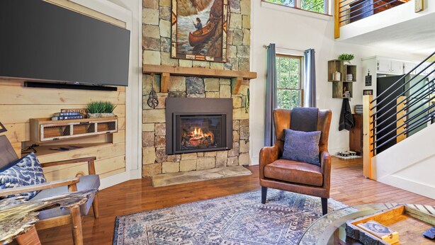 A spacious living room with a stone fireplace, a mounted television, and a comfortable seating area. - Creekfront! 5* Views, hot tub, fire pit, huge deck (Blue Ridge)