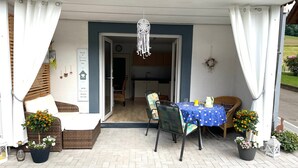 Une terrasse extérieure avec une table recouverte d’une nappe bleue, des meubles en osier et des plantes en pot.