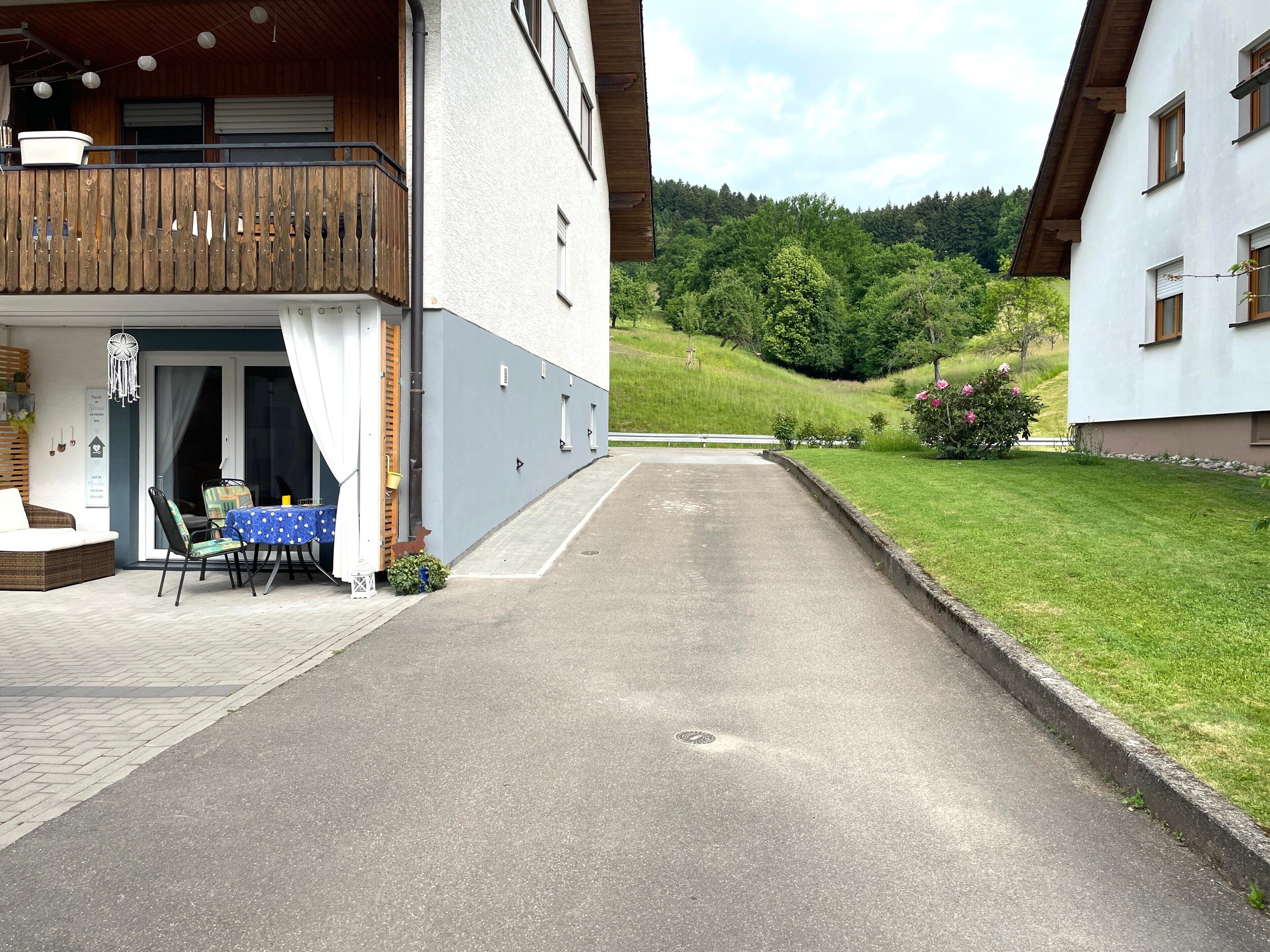 Un bâtiment doté d’un balcon, une table avec des chaises à l’extérieur, et une allée pavée menant à une zone herbeuse.