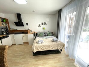 Une chambre d’hôtel moderne dotée d’un lit, d’une kitchenette et de grandes fenêtres.
