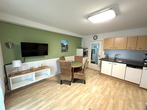 Un espace de vie compact comprenant un coin repas, une kitchenette et un téléviseur fixé au mur.