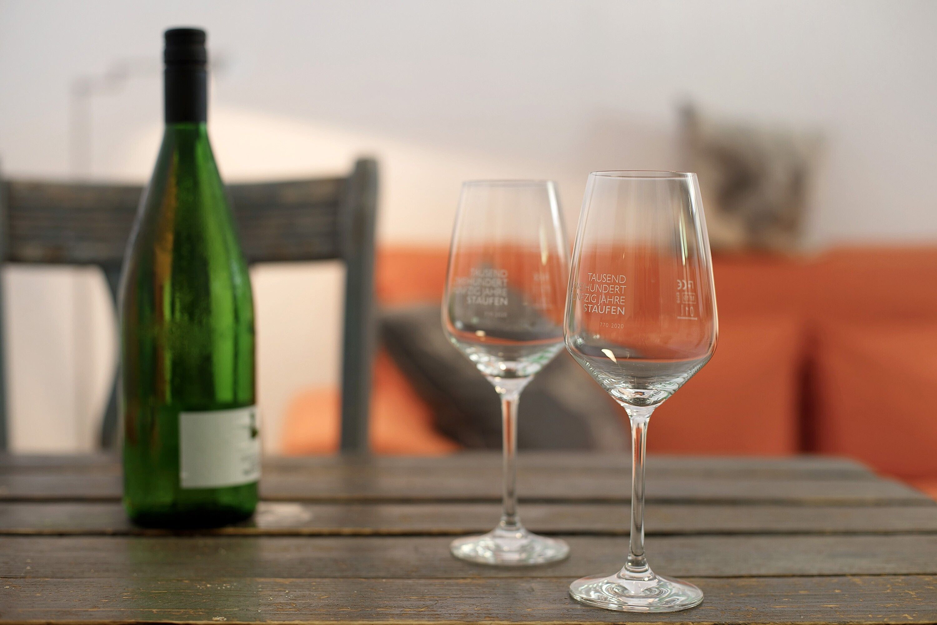 Une bouteille de vin verte et deux verres à vin vides sur une table en bois.
