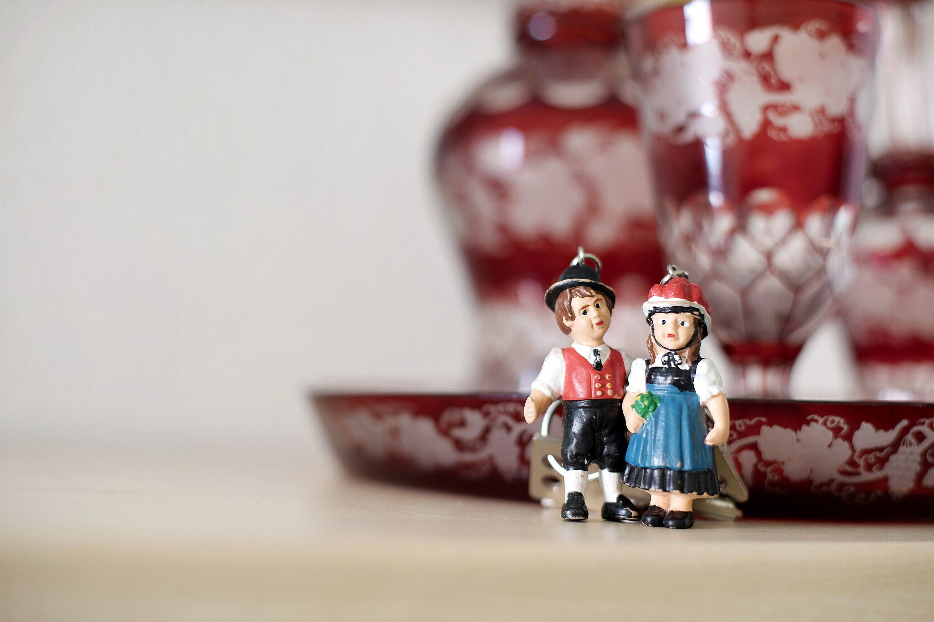 Eine Figur eines Mannes und einer Frau in traditioneller Kleidung, ein rotes und weißes Keramikgefäß mit Muster und eine kleine, rot-weiße Schale mit Muster.