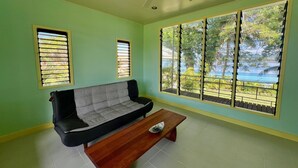 Una habitación con sofá, banco de madera y ventanas grandes con persianas.