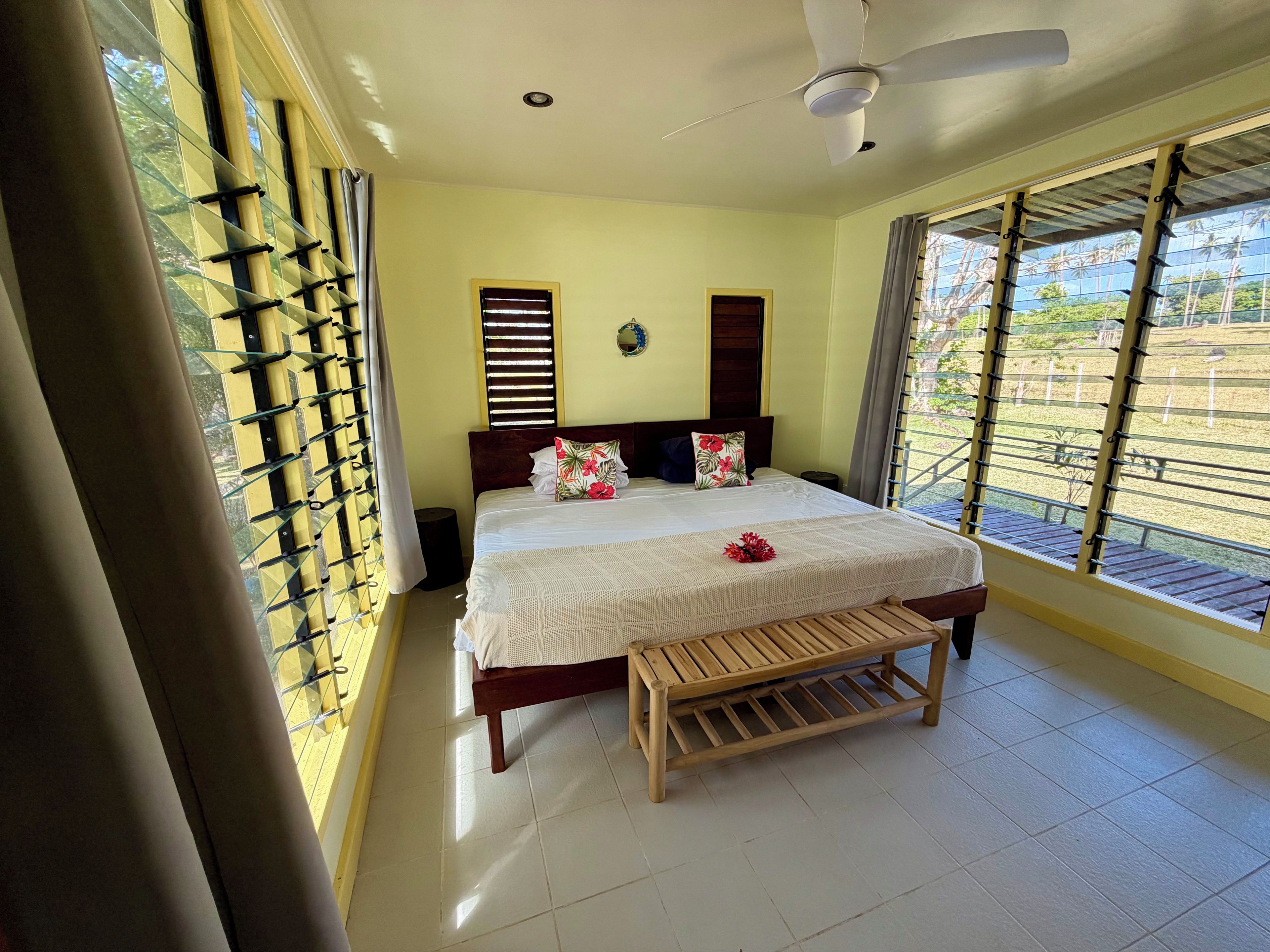 Une chambre d’hôtel avec un lit, un ventilateur de plafond, une fenêtre avec des stores et une vue sur l’extérieur.