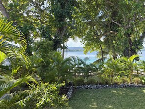 Un jardin luxuriant, où s’épanouissent de nombreuses plantes tropicales, et qui offre une vue sur une étendue d’eau paisible.