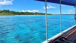 A boat with a blue canopy and wooden benches, sailing on clear blue waters with a beach and trees in the background. - Private Beachfront Paradise on Aore Island (Aore Island)