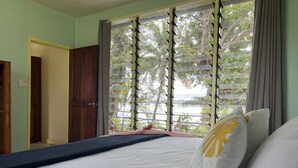 A room with a bed, a window with blinds, a door, and a view of greenery outside. - Private Beachfront Paradise on Aore Island (Aore Island)