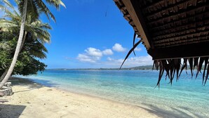 A beach with clear turquoise water, palm trees, and a wooden structure. - Private Beachfront Paradise on Aore Island (Aore Island)