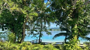 A lush garden with a wooden deck overlooking a calm lake, surrounded by dense foliage and tropical plants. - Private Beachfront Paradise on Aore Island (Aore Island)