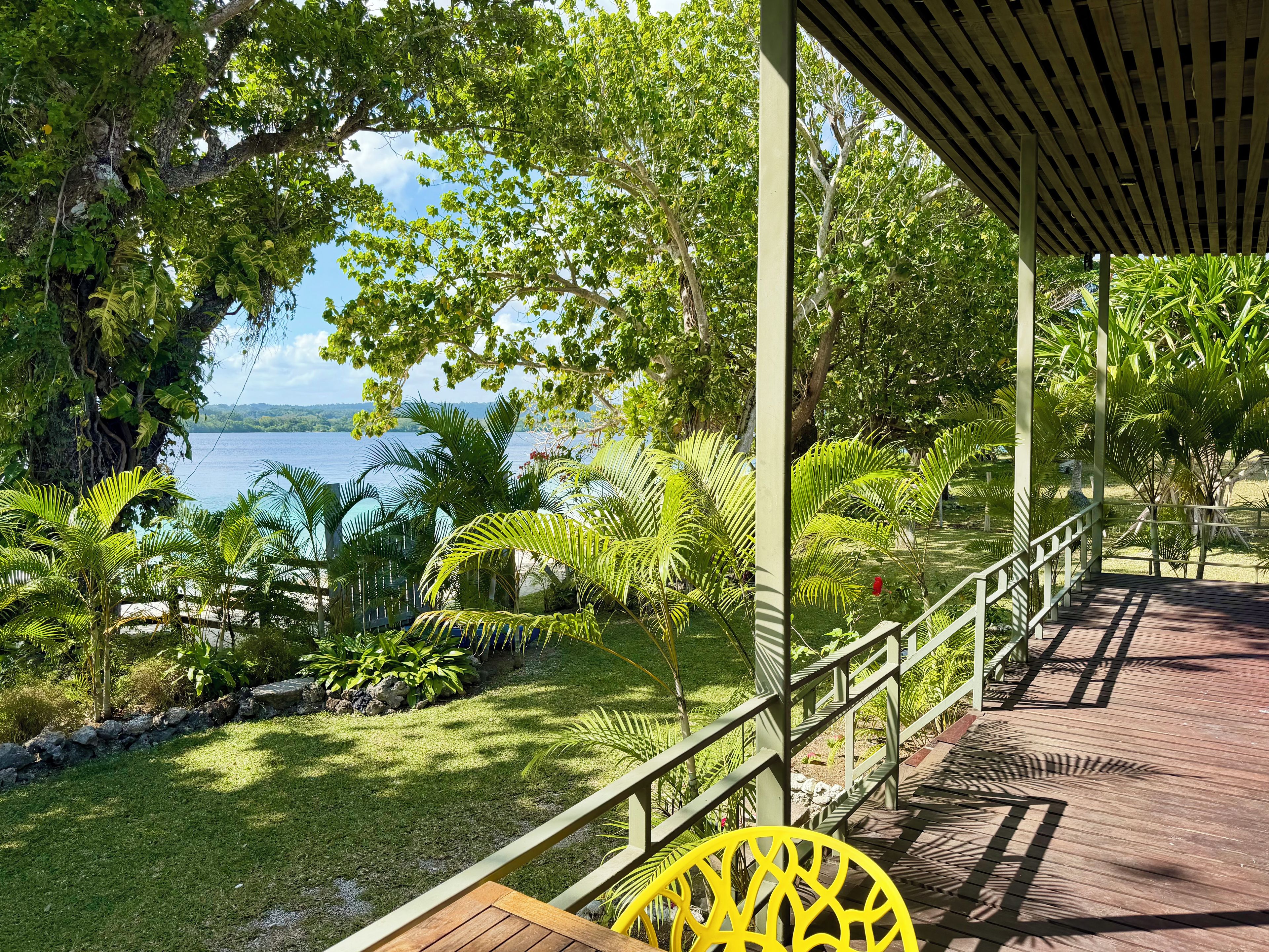 A covered outdoor area with a wooden deck, a yellow chair, and a view of a body of water.