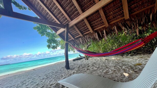 A beach with a hammock and a mat under a thatched roof structure. - Private Beachfront Paradise on Aore Island (Aore Island)